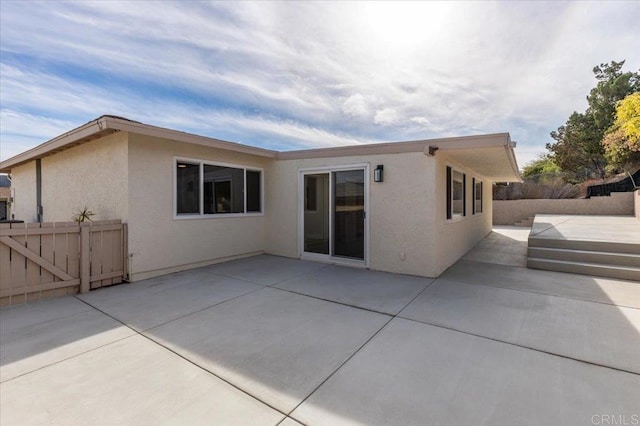 rear view of house with stucco siding, a patio, and fence