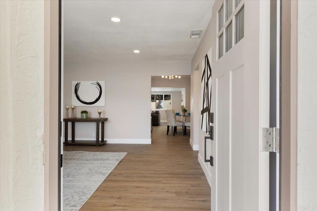 hallway featuring baseboards, wood finished floors, visible vents, and recessed lighting