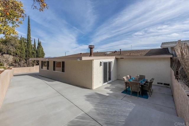 rear view of house with outdoor dining space, a patio, and stucco siding