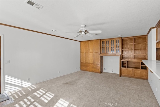 unfurnished living room with ceiling fan, light carpet, crown molding, and built in desk