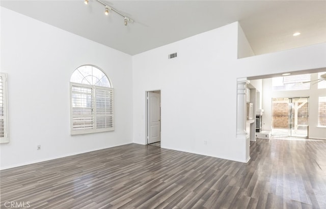 empty room with dark wood-type flooring, track lighting, and a towering ceiling