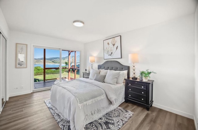 bedroom with a water view, dark wood-type flooring, and access to exterior