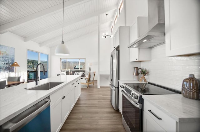 kitchen featuring sink, hanging light fixtures, stainless steel appliances, light stone countertops, and wall chimney range hood