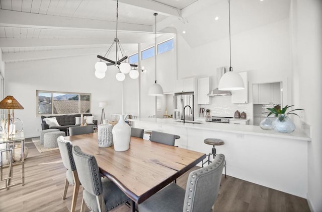 dining area with high vaulted ceiling, beamed ceiling, sink, an inviting chandelier, and light hardwood / wood-style flooring