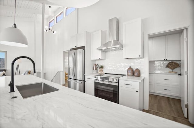 kitchen with pendant lighting, wall chimney range hood, sink, stainless steel appliances, and white cabinets