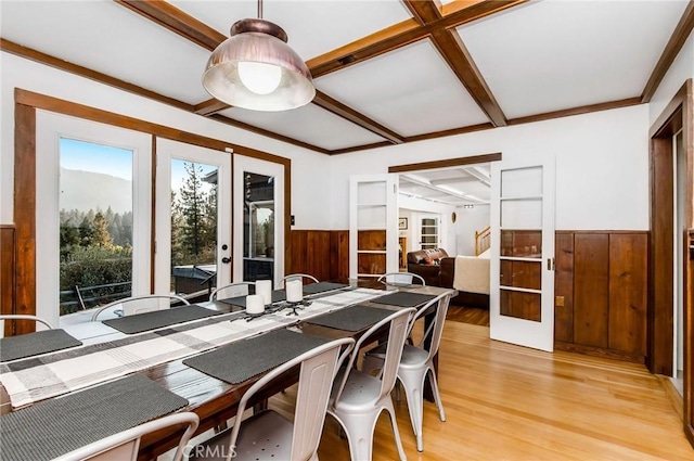 dining room featuring beamed ceiling, light hardwood / wood-style flooring, wood walls, and french doors