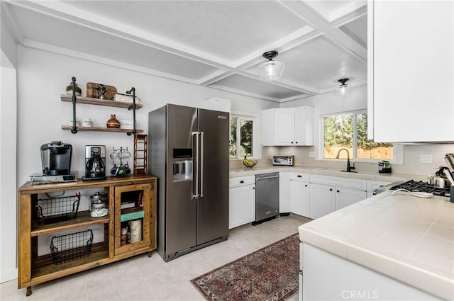 kitchen with appliances with stainless steel finishes, white cabinets, plenty of natural light, coffered ceiling, and tile counters