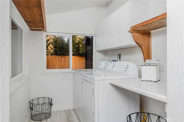 clothes washing area featuring cabinets, washing machine and dryer, and light wood-type flooring