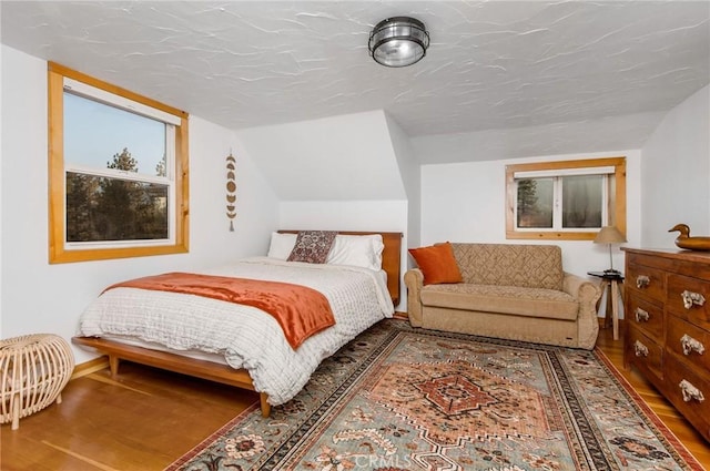 bedroom with wood-type flooring, a textured ceiling, and vaulted ceiling