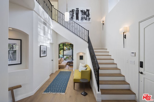 staircase with wood-type flooring and a towering ceiling