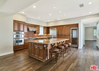 kitchen with a breakfast bar, stainless steel appliances, dark hardwood / wood-style floors, an island with sink, and wall chimney exhaust hood