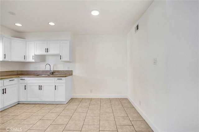 kitchen with light tile patterned floors, sink, and white cabinets