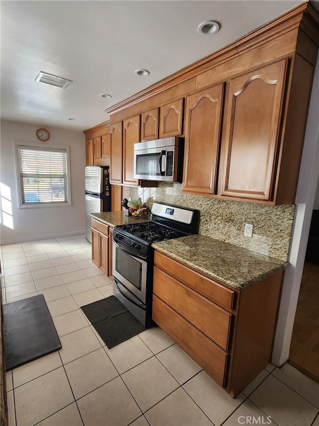 kitchen featuring tasteful backsplash, appliances with stainless steel finishes, light tile patterned floors, and dark stone counters