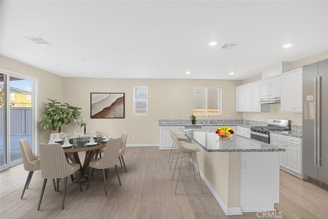 kitchen featuring white cabinets, a center island, stainless steel appliances, light hardwood / wood-style floors, and light stone counters