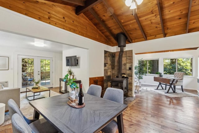 dining room featuring a wood stove, beam ceiling, wooden ceiling, and light wood-type flooring