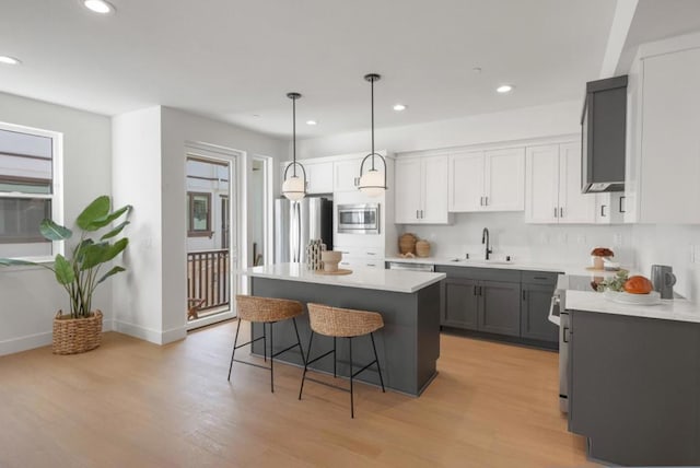 kitchen with gray cabinets, stainless steel appliances, a kitchen island, decorative light fixtures, and light wood-type flooring