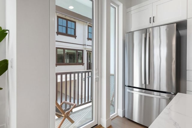 kitchen with stainless steel refrigerator, white cabinetry, light stone countertops, and a wealth of natural light