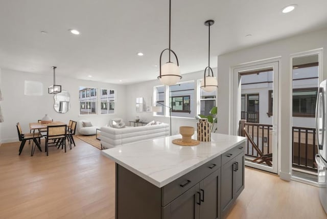 kitchen featuring hanging light fixtures, light hardwood / wood-style flooring, light stone countertops, and a kitchen island