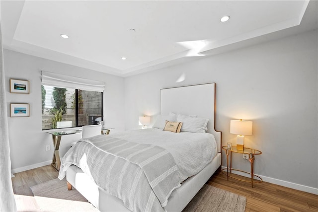 bedroom with wood-type flooring and a tray ceiling