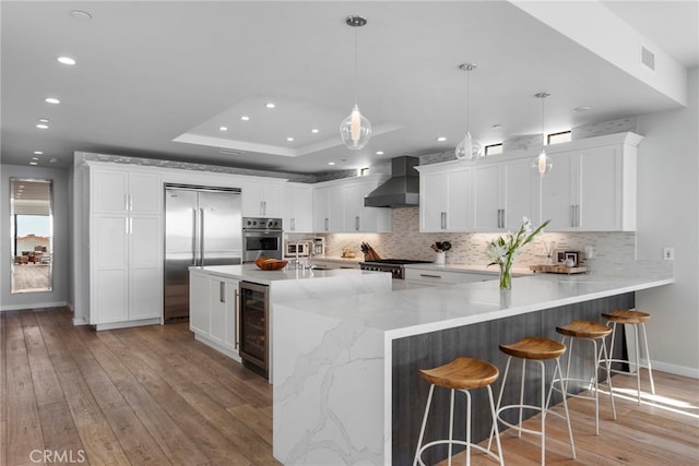 kitchen featuring white cabinetry, pendant lighting, wall chimney range hood, and stainless steel appliances