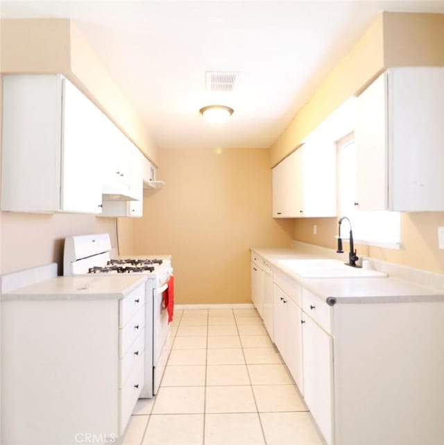 kitchen featuring sink, white gas range oven, white cabinets, and light tile patterned flooring