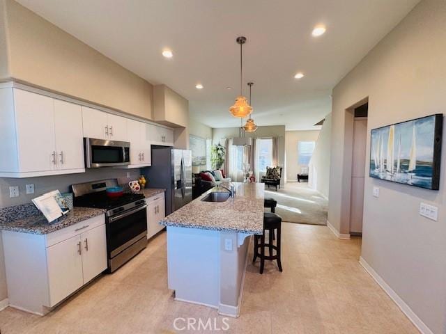 kitchen with pendant lighting, white cabinetry, a center island with sink, and stainless steel appliances