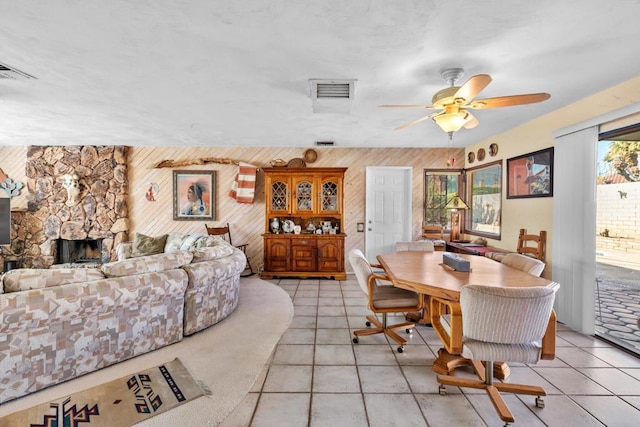 tiled dining room with ceiling fan, a fireplace, and wooden walls