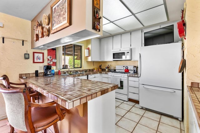 kitchen featuring white cabinetry, white appliances, kitchen peninsula, and tile countertops