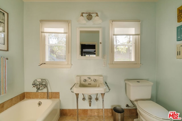 bathroom featuring toilet, a healthy amount of sunlight, sink, and a tub to relax in