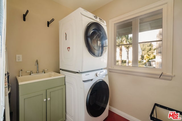 laundry area featuring cabinets, stacked washing maching and dryer, and sink