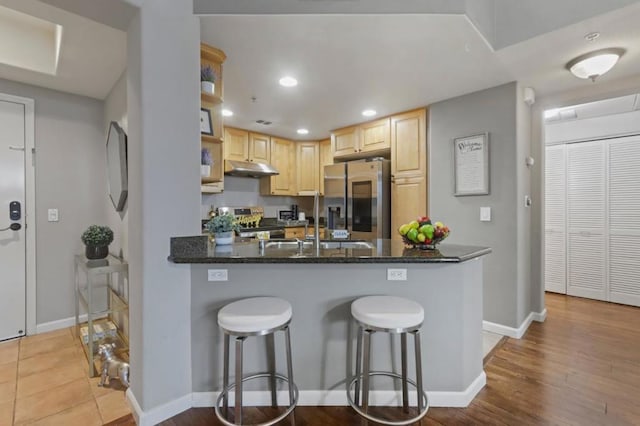 kitchen featuring appliances with stainless steel finishes, sink, dark stone countertops, kitchen peninsula, and light brown cabinets