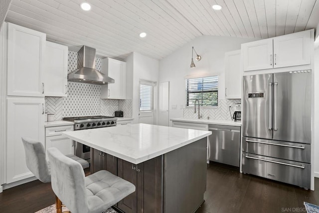 kitchen with premium appliances, white cabinets, lofted ceiling, wall chimney exhaust hood, and a kitchen island