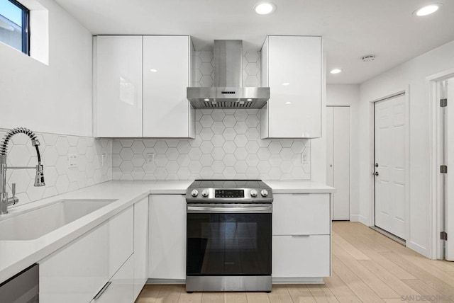 kitchen with white cabinetry, wall chimney range hood, sink, stainless steel electric stove, and backsplash