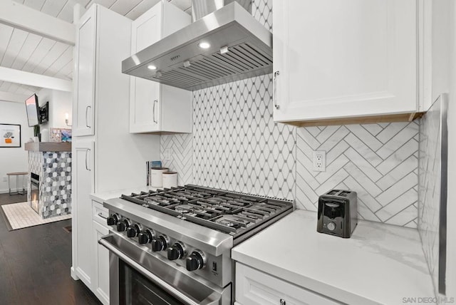 kitchen with tasteful backsplash, extractor fan, beam ceiling, white cabinetry, and stainless steel range