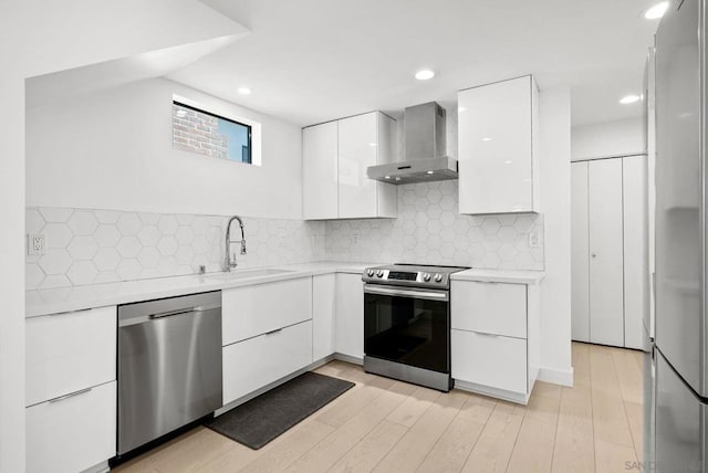 kitchen with appliances with stainless steel finishes, wall chimney exhaust hood, sink, white cabinets, and decorative backsplash