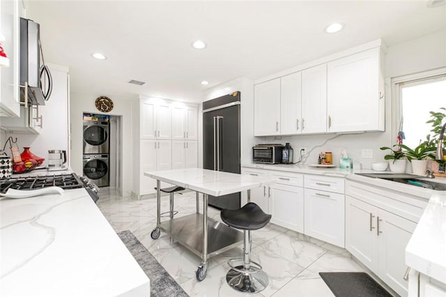 kitchen with built in fridge, a kitchen island, white cabinetry, stacked washer and clothes dryer, and a breakfast bar