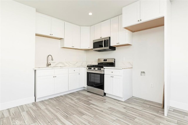 kitchen with sink, white cabinets, light hardwood / wood-style floors, and appliances with stainless steel finishes