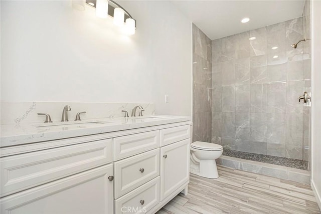 bathroom with a tile shower, toilet, and vanity