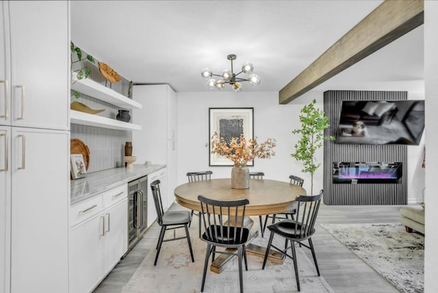 dining area with a notable chandelier, beverage cooler, light wood-type flooring, and a fireplace