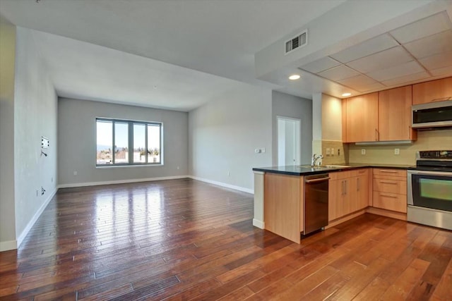 kitchen with kitchen peninsula, light brown cabinetry, dark hardwood / wood-style flooring, sink, and stainless steel appliances