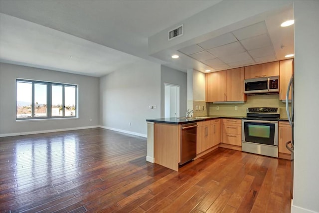 kitchen with light brown cabinetry, sink, kitchen peninsula, dark wood-type flooring, and stainless steel appliances