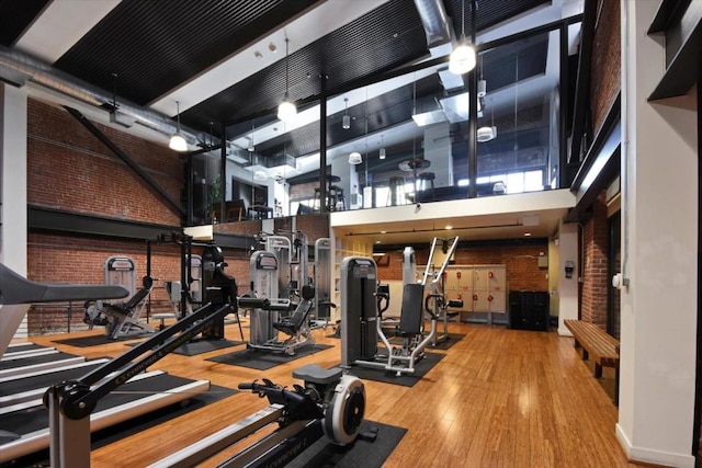 workout area with a towering ceiling, hardwood / wood-style flooring, and brick wall