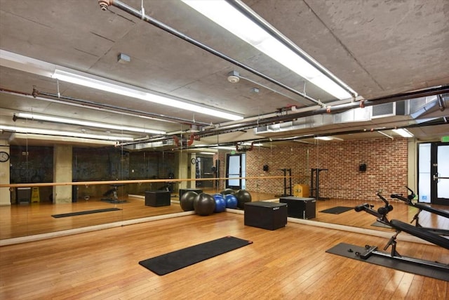 exercise room featuring hardwood / wood-style flooring and brick wall