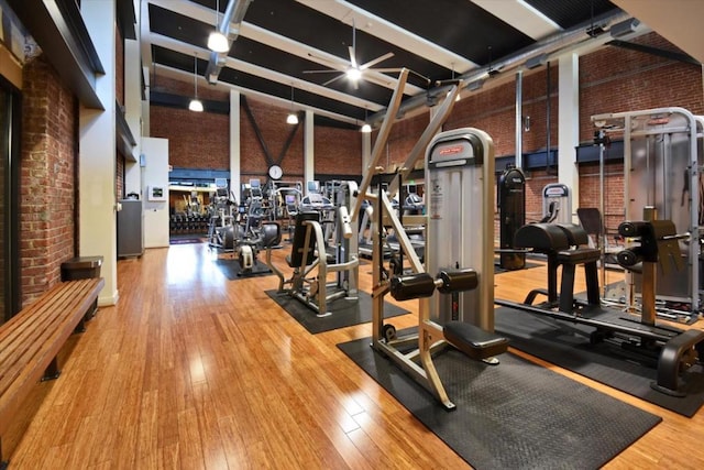 exercise room with brick wall, high vaulted ceiling, and hardwood / wood-style floors