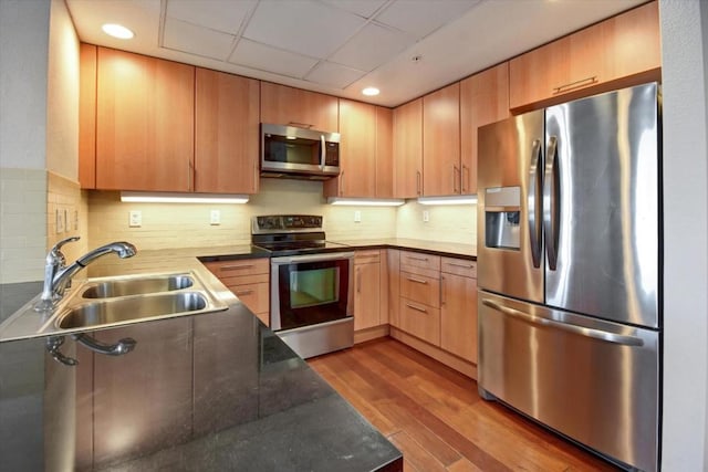 kitchen with sink, light brown cabinets, light wood-type flooring, appliances with stainless steel finishes, and decorative backsplash