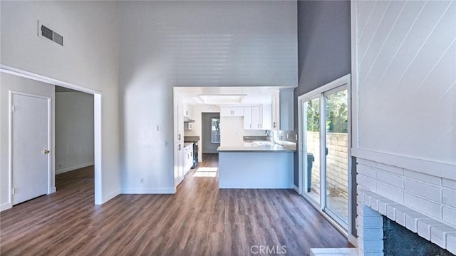 interior space with dark wood-type flooring, a high ceiling, white cabinets, and kitchen peninsula