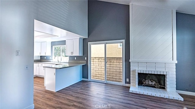 kitchen with kitchen peninsula, sink, white cabinetry, a towering ceiling, and a fireplace