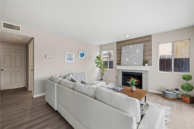 living room with a brick fireplace and dark wood-type flooring