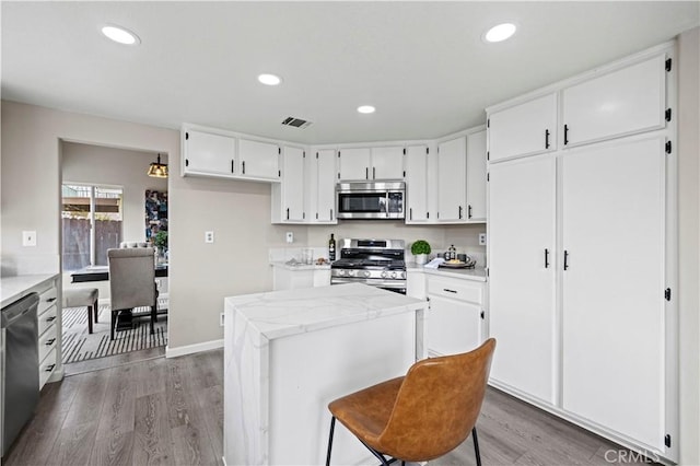 kitchen featuring hardwood / wood-style flooring, white cabinetry, stainless steel appliances, light stone countertops, and a kitchen island