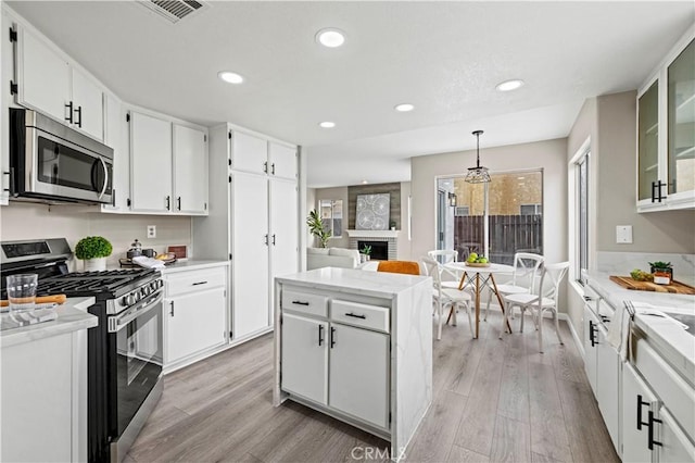 kitchen with white cabinetry, a center island, hanging light fixtures, appliances with stainless steel finishes, and light hardwood / wood-style floors